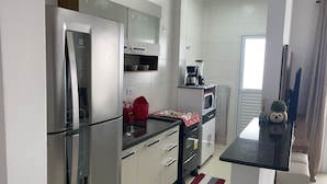 A modern kitchen with stainless steel appliances, white cabinets, and a black countertop. - Excelente Apto com piscina em Praia Grande (Praia Grande)