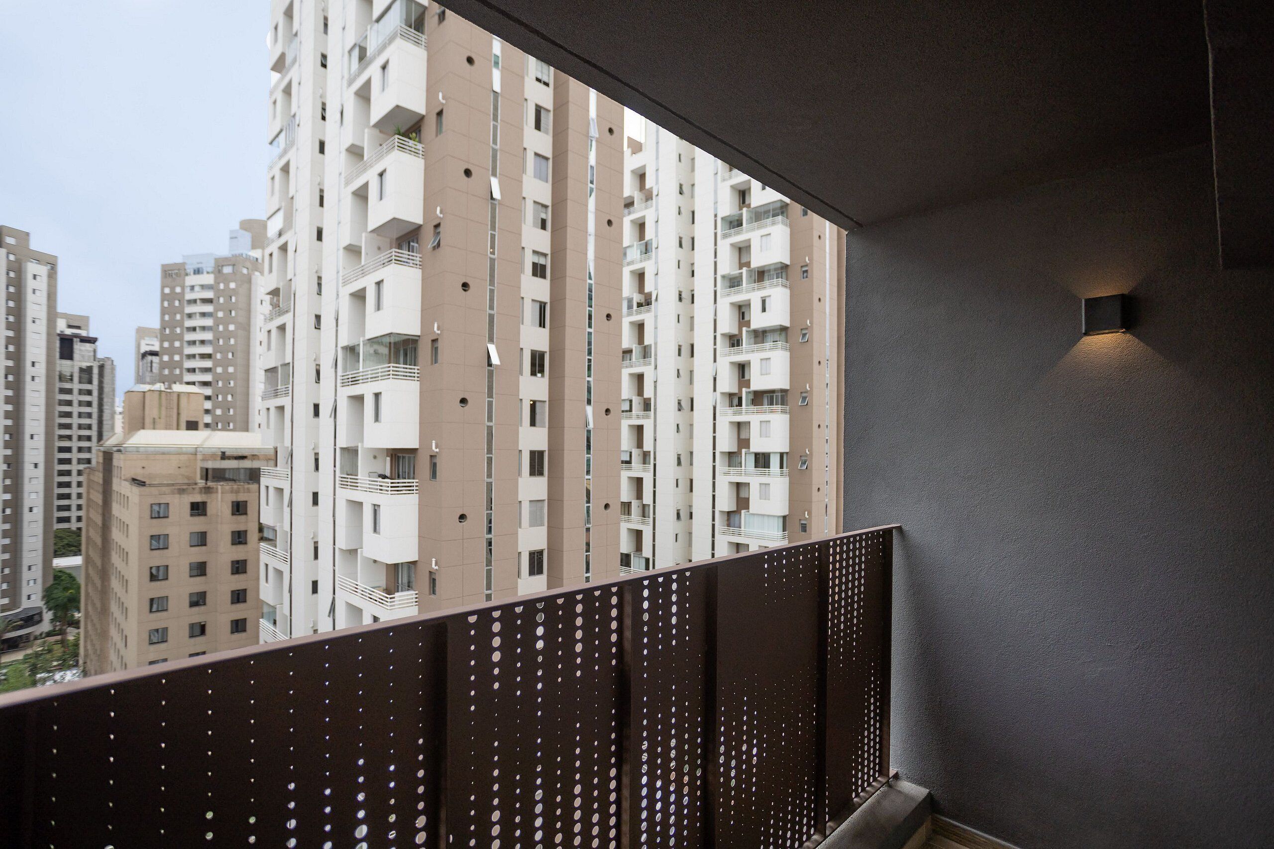 Um edifício alto com várias varandas, um design moderno de guarda-corpo e um pequeno acessório de iluminação fixado na parede.