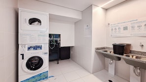 Ein modernes Badezimmer mit integrierter Waschmaschine und Trockner, einem Granitwaschbecken und Informationspostern an den Wänden.