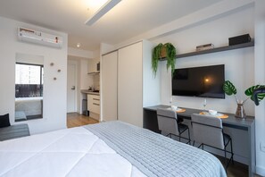 Ein modernes Hotelzimmer mit einem Bett, einem Schreibtisch mit zwei Stühlen, einem Fernseher und einer kleinen Küchenzeile.