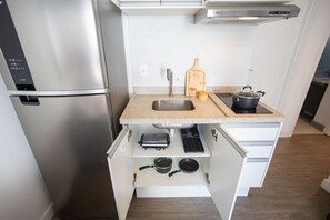 A compact kitchen with a stainless steel refrigerator, a sink, a wooden cutting board, a pot, and a toaster.