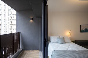 A modern bedroom with a large bed, a dark-colored wall, and a window overlooking a building.