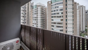Un balcón con vistas a edificios altos, un equipo de aire acondicionado y una barandilla de metal perforado.