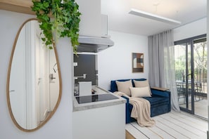 A modern living room with a blue sofa, a kitchen area with a built-in stove, and a large mirror. - Walk Moema (São Paulo)
