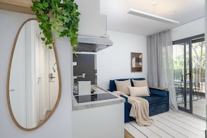 Uma sala de estar moderna com um sofá azul, uma área de cozinha com fogão embutido e um espelho grande.