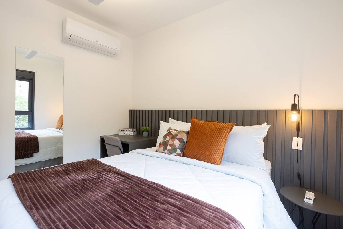 Ein modernes Hotelzimmer mit einem großen Bett, einem Nachttisch mit Lampe und einer wandmontierten Klimaanlage.
