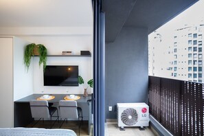 A modern hotel room with a balcony, a flat-screen TV, a dining area, and an air conditioning unit. - Walk Moema (São Paulo)