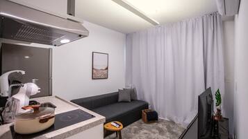 Uma sala de estar moderna com sofá, televisão de tela plana, espaço de cozinha com fogão e mesa de jantar.