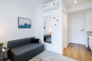 A modern living room with a grey sofa, a mounted picture, a mirror, and a small table with a plant. - Walk Moema (São Paulo)