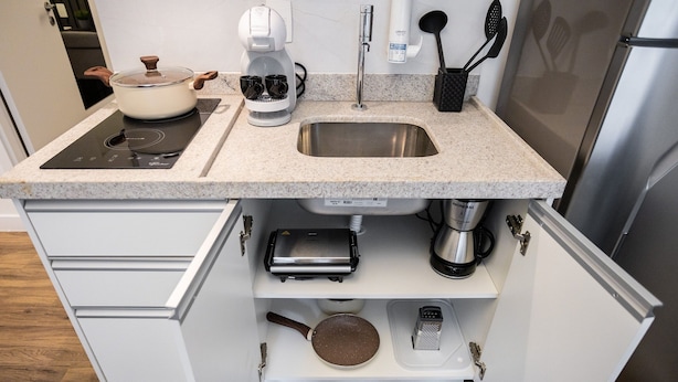 Una cocina con placa de inducción integrada, cafetera, tostadora y un lavamanos de acero inoxidable.