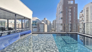 Ein Pool auf dem Dach mit Glasbarriere, der einen Blick auf umliegende Hochhäuser bietet.