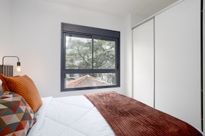 Quarto com cama, janela e mesa de cabeceira com abajur.