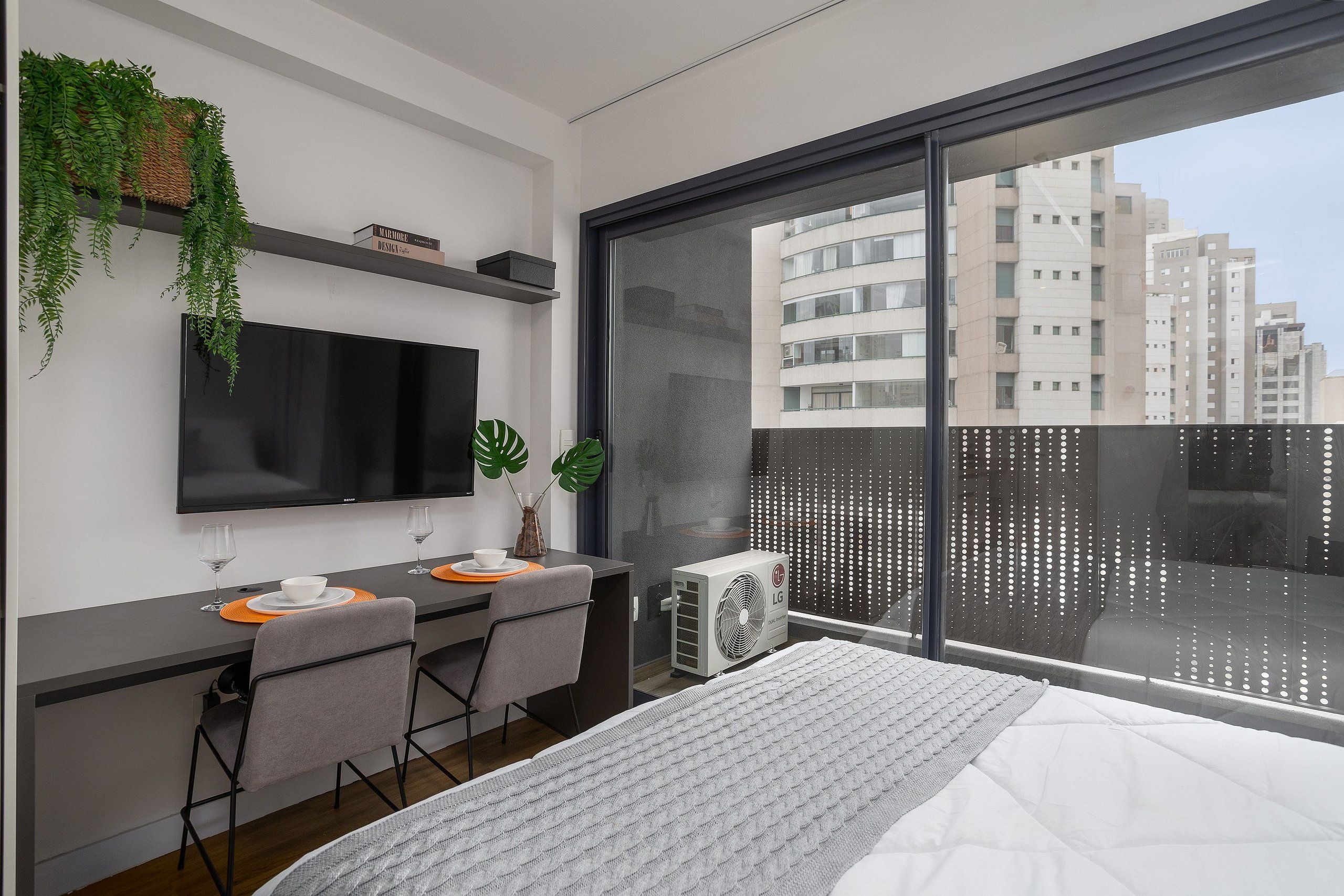 Une chambre moderne avec un grand lit, un bureau avec deux chaises, un téléviseur à écran plat et un appareil de climatisation.