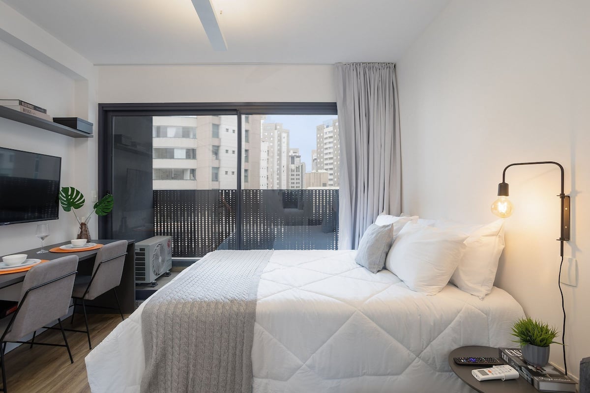Ein modernes Hotelzimmer mit einem großen Bett, einem Schreibtisch mit Computer, einem Fernseher und einem Balkon mit Blick auf die Stadt.