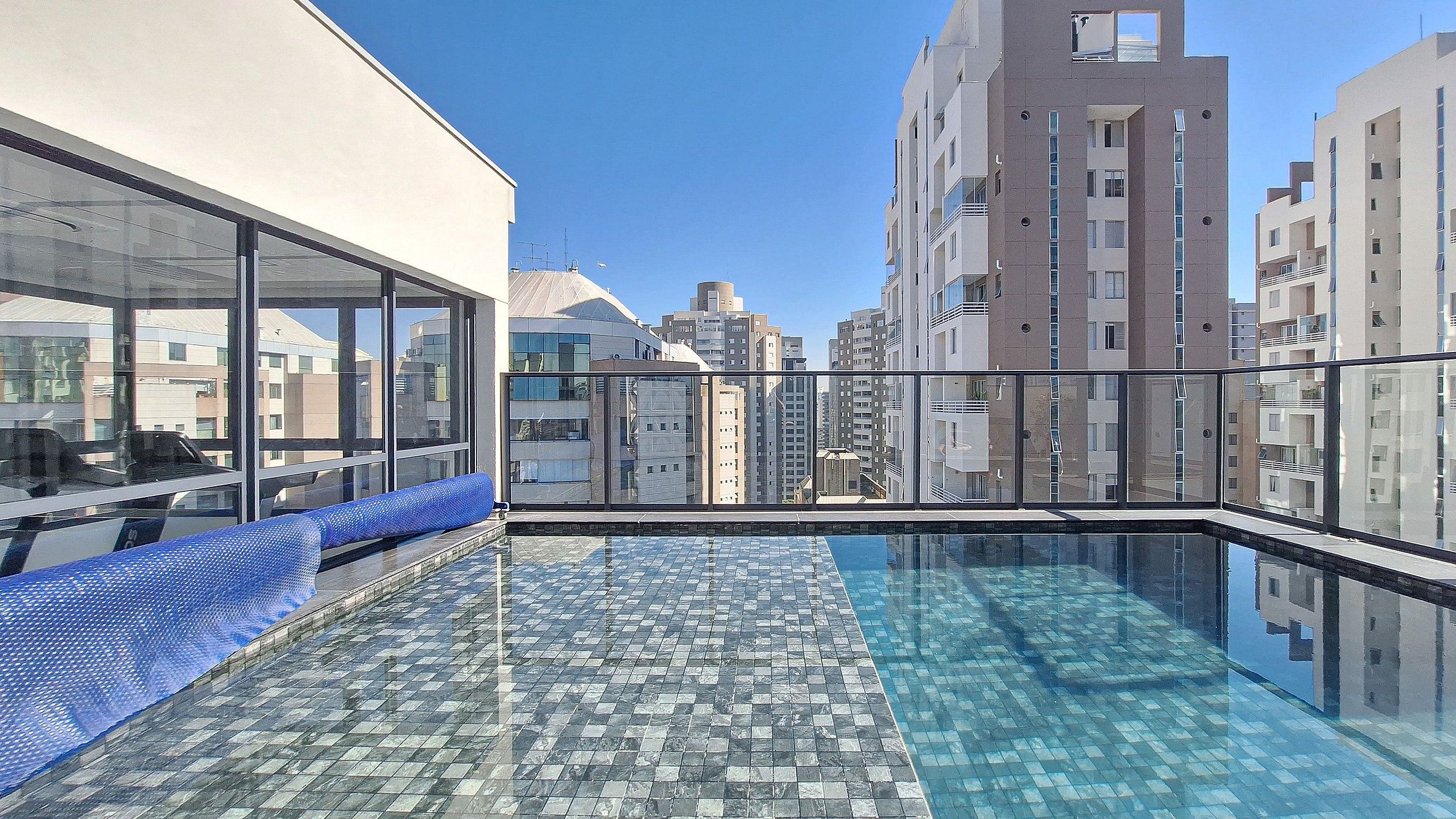 A rooftop pool with a glass barrier, offering a view of surrounding high-rise buildings.