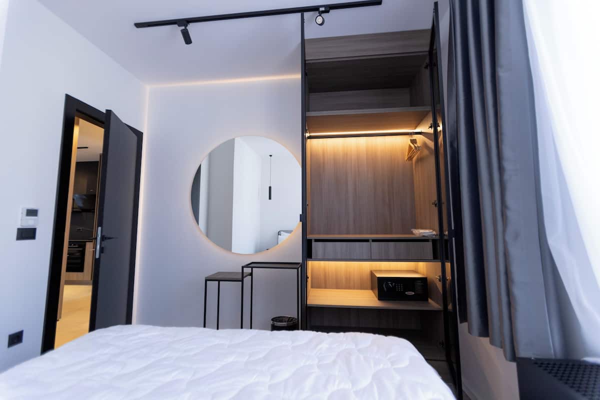 A modern hotel room with a bed, a mirror, a built-in wardrobe, and a small desk.