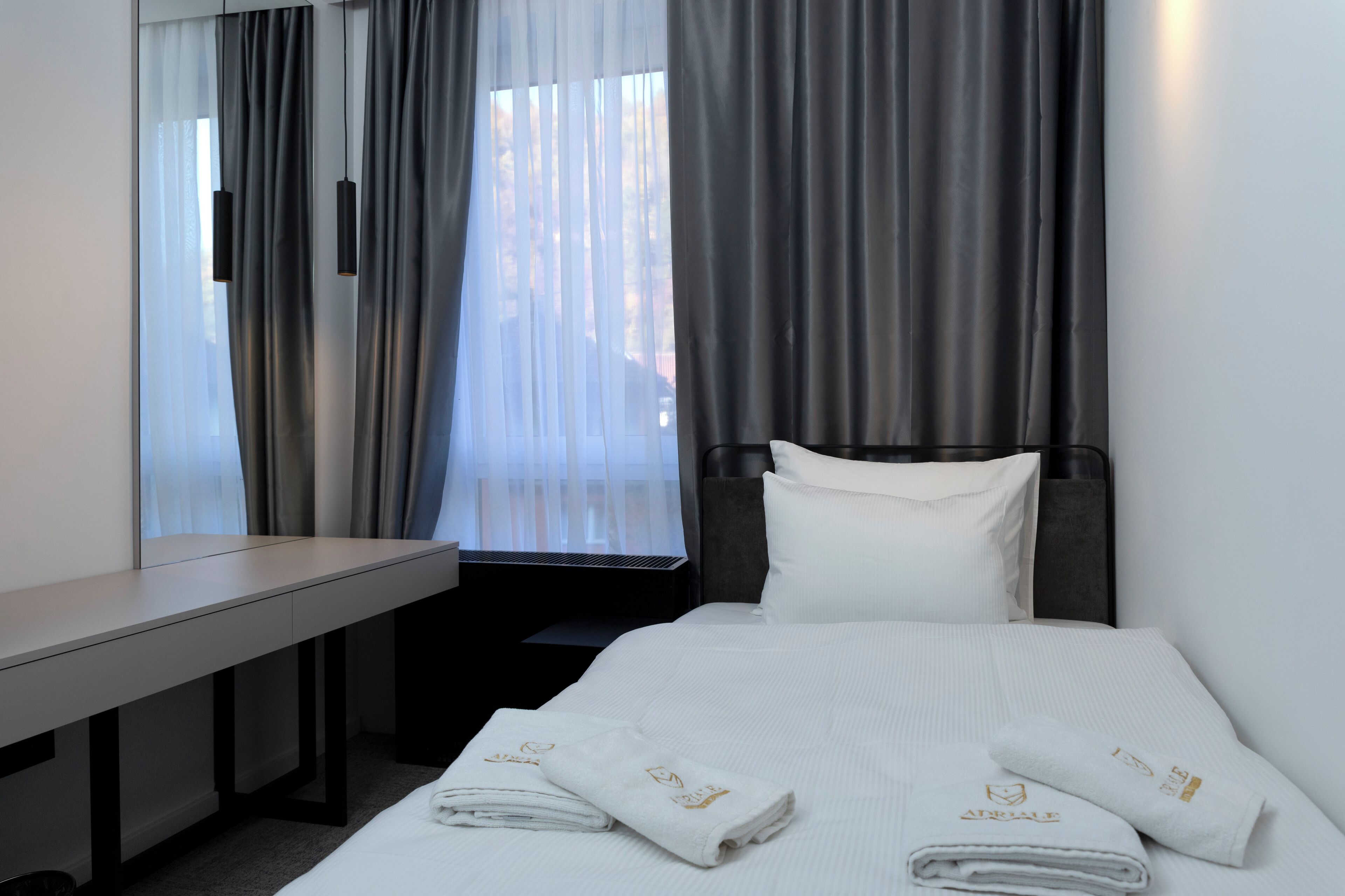 A hotel room with a bed, a desk, and a window with curtains.