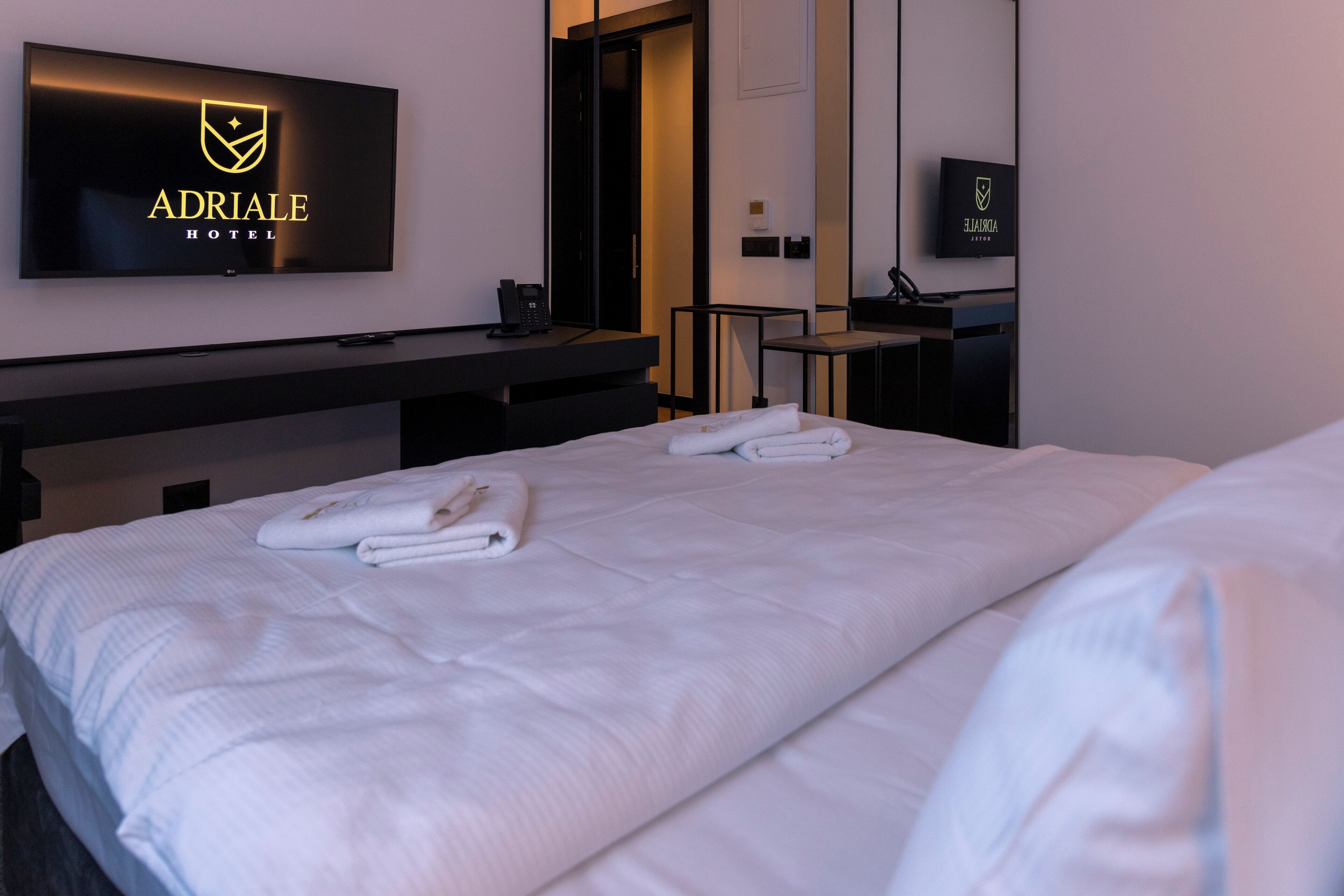 A hotel room with a large bed, a desk, a chair, and a flat-screen TV mounted on the wall.