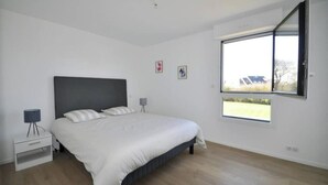 Une chambre à coucher avec un grand lit, une table de chevet, une lampe et une fenêtre donnant sur l’extérieur.