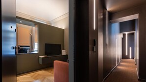 A modern hotel room with a wooden herringbone floor, a flat-screen TV, a small seating area, and a large mirror. - Lagrange Design Apartment by Wonderful Italy - Alfa (Turin)
