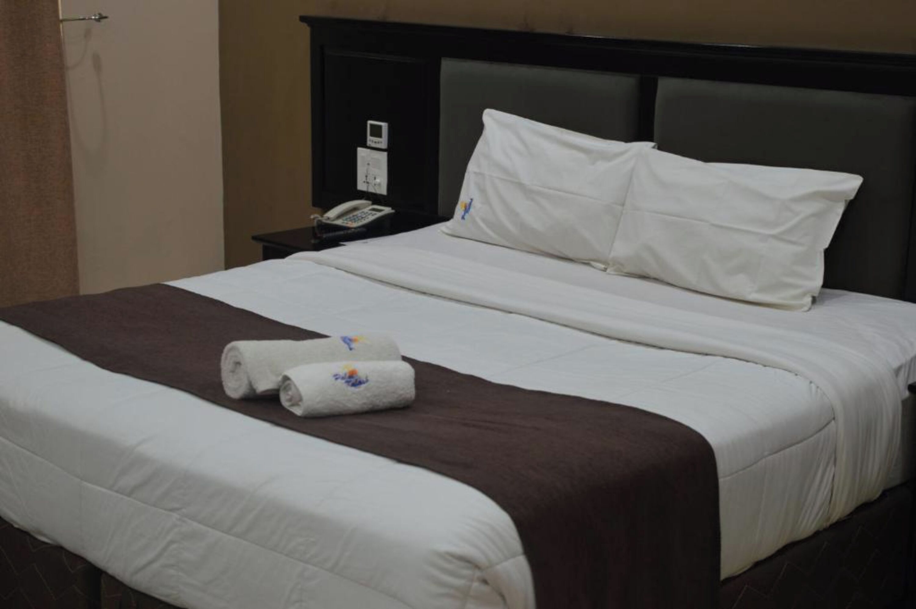 A hotel room with a neatly made bed, a bedside telephone, and a brown headboard.