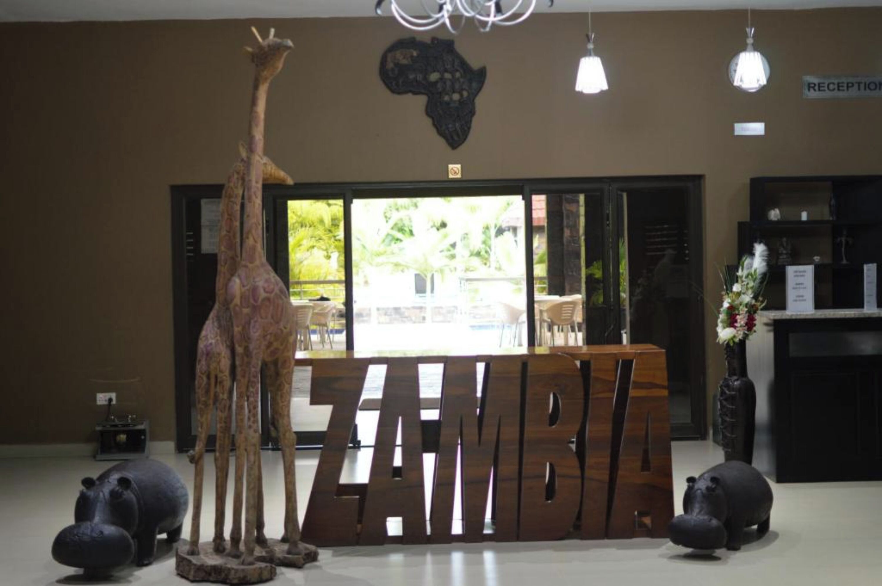 Et receptionsområde med et stort skilt med teksten 'ZAMBIA', en girafskulptur og hippopotamusser.