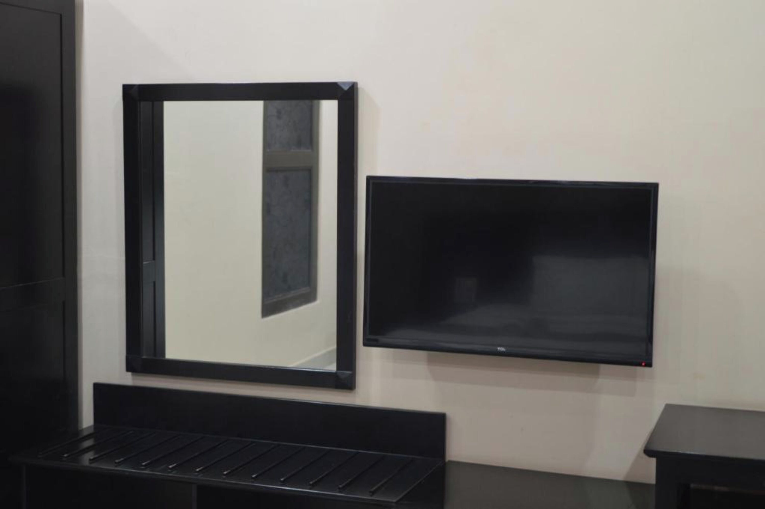 Une pièce avec un miroir à cadre noir et un téléviseur à écran plat fixé au mur.