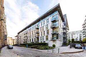 A modern apartment building with multiple balconies, a cobblestone street, and a pedestrian walkway. - City-Close 1-Bed Apartment near Tower Hill (London)