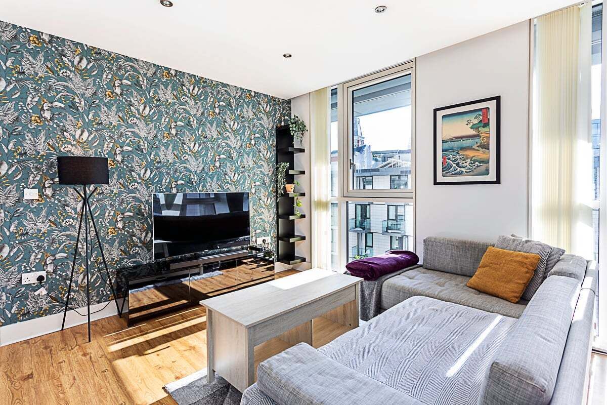 A modern living room with a large flat-screen TV, a sofa, a coffee table, and a patterned wallpaper.