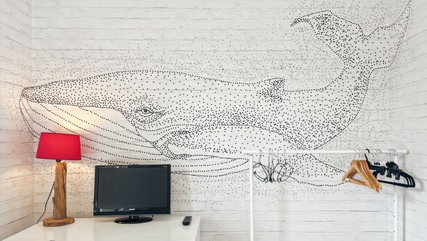 Una habitación con pared de ladrillo blanco, un escritorio con computadora, una lámpara roja y un perchero.
