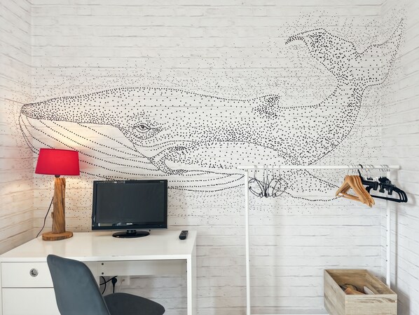 A room with a white brick wall, a desk with a computer, a red lamp, and a hanging coat rack.