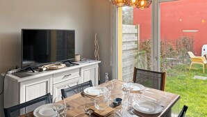 Comedor con televisor, mesa de madera, sillas y puerta de cristal que da a un jardín.