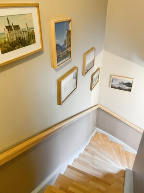 A staircase with wooden steps and a handrail, leading to a landing with framed pictures on the wall.