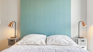 Una cama con ropa de cama blanca, dos mesitas de noche con lámparas y un cabecero color turquesa.