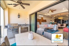 A spacious living area with a large sofa, a coffee table, and a dining table. There is a grill and a refrigerator in the kitchen area. - CCV Quivira - Luxurious 2BR w/ Ocean Views and Golf access! (Cabo San Lucas)