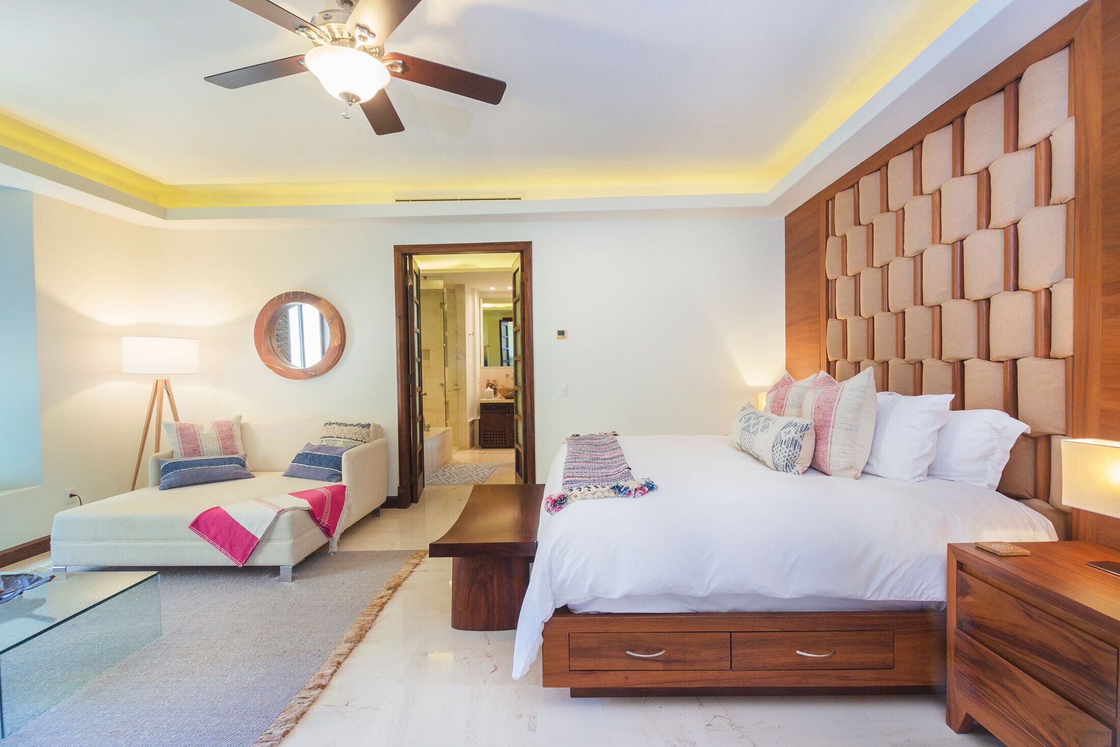 A modern bedroom with a bed, bedside tables, a ceiling fan, and a mirror.