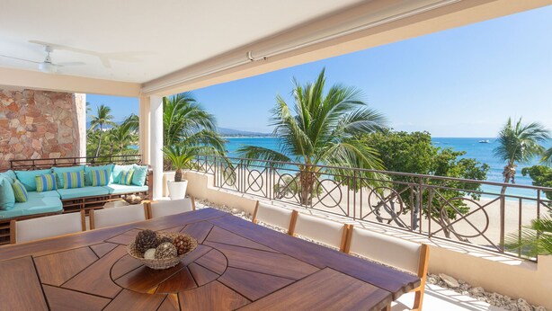A wooden dining table with a decorative centerpiece, a light blue sofa with striped cushions, and a view of the ocean and palm trees. - Calm and Cosy 4 Bedroom Condo (Punta de Mita)