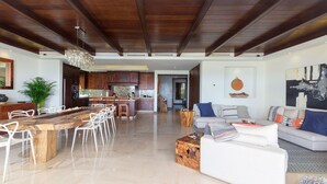 A spacious living area with a wooden dining table, white chairs, a sofa set, and a kitchen in the background. - Calm and Cosy 4 Bedroom Condo (Punta de Mita)