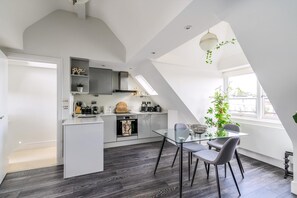 Ett modernt kök med ett glasbord, grå stolar och ett takfönster.
