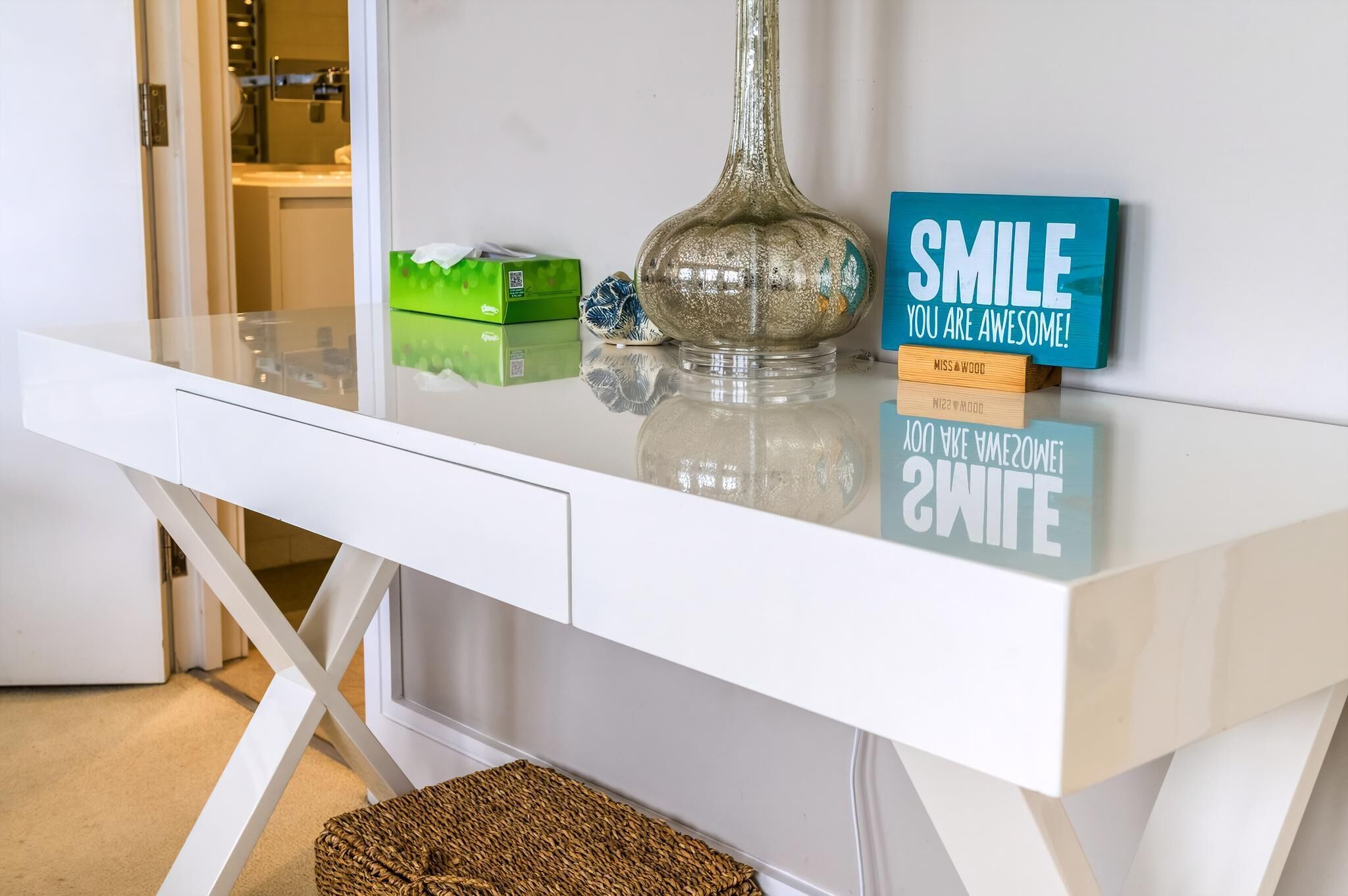 A white desk with a glass vase, a green box, and motivational signs.