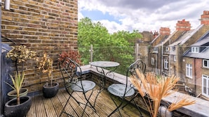 A balcony with a wooden floor, potted plants, metal chairs, and a table. - Gorgeous Hampstead Flat (London)
