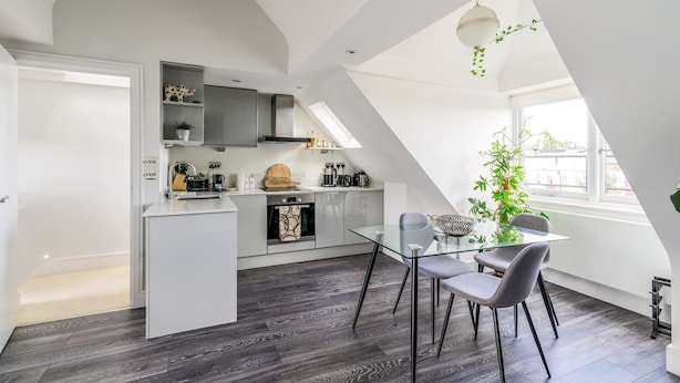A modern kitchen with a glass dining table, grey chairs, and a view of the city through large windows. - Gorgeous Hampstead Flat (London)