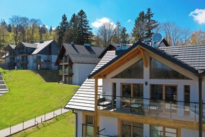 Ein modernes, mehrstöckiges Gebäude mit großen Fenstern, einem Balkon und einem geneigten Dach.