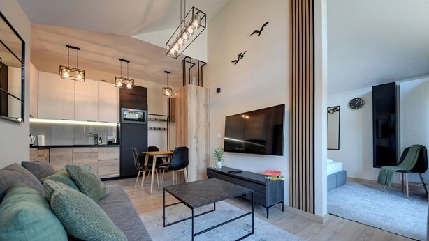 A modern living space with a sofa, coffee table, TV, and kitchen area. - RentPlanet - Osada Górska (Szklarska Poreba)