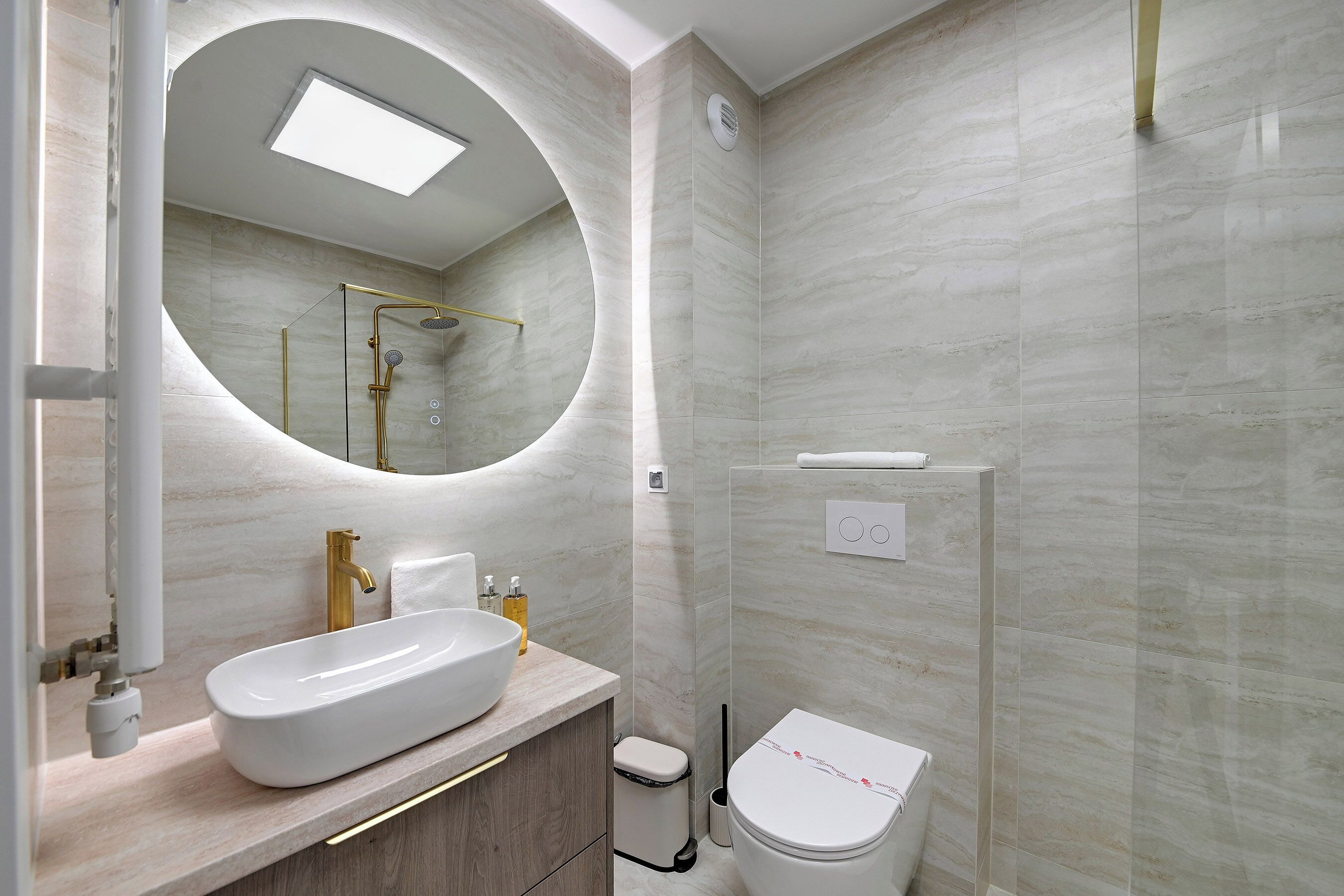 Een moderne badkamer met een grote ovale spiegel, een wit wastafelmeubel, een toilet en een douchecabine.