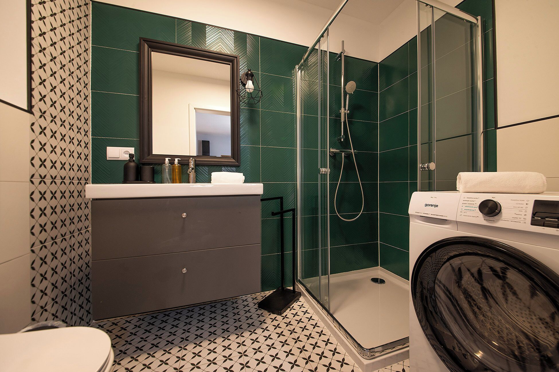 Un baño moderno con cabina de ducha de vidrio, lavadora y azulejos estampados.