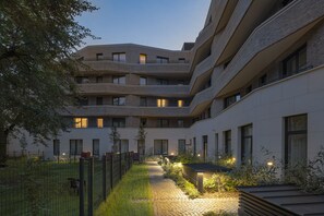 A multi-story building with a courtyard, featuring a brick facade, multiple windows, and a pathway leading to a seating area. - Elisapart - Apartments am Sommerschloss (Potsdam)