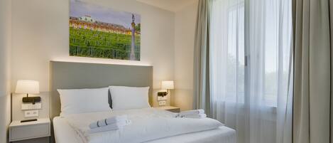 A hotel room with a neatly made bed, two bedside tables with lamps, a painting on the wall, and a large window with curtains.