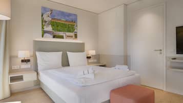 Une chambre d’hôtel moderne avec un lit soigneusement fait, un tableau au-dessus du lit, un téléviseur posé sur un meuble et une porte sur le côté droit.