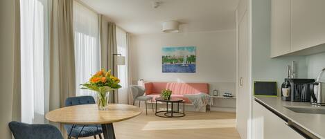A modern living room with a round wooden table, two blue chairs, a pink sofa, and a painting on the wall.